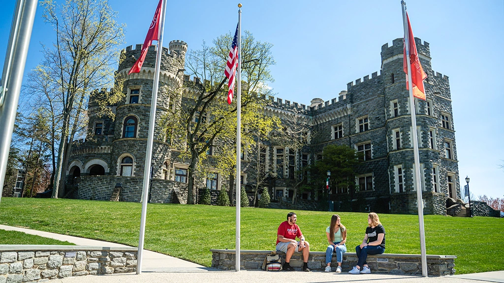 Three students sit on a ledge in front of the castle with flags at a standstill.