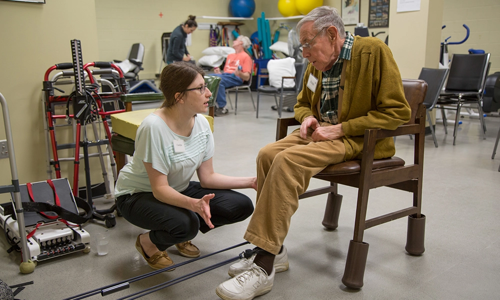 A physical therapist talks to an older adult as he sits during an exam.