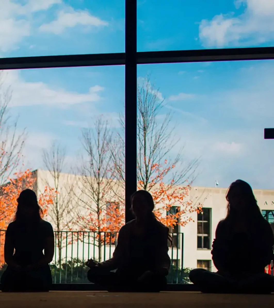The silhouettes of three students in front of the Landman Library on campus.