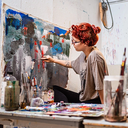 An Arcadia art student work on a a large painting on canvas in a studio.