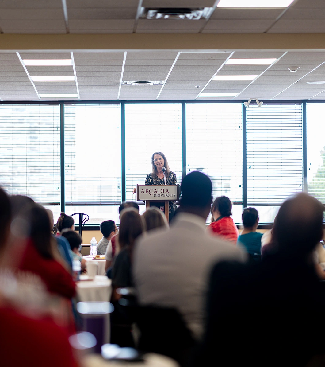 A speaker sands in front of a crowd at the Honors Breakfast event.