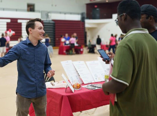 An Arcadia University faculty member visits an event table during an open house.