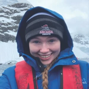 Aoife Samuelson '24 smiles for a selfie in Antarctica wearing an Arcadia Knights beanie