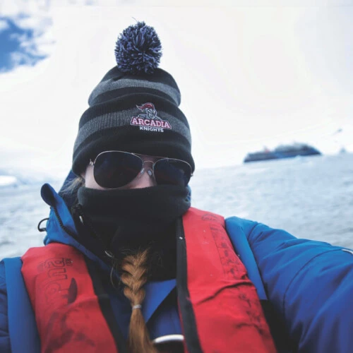 Aoife Samuelson '24 takes a selfie in Antarctica wearing an Arcadia Knights winter hat, mask and sunglasses.