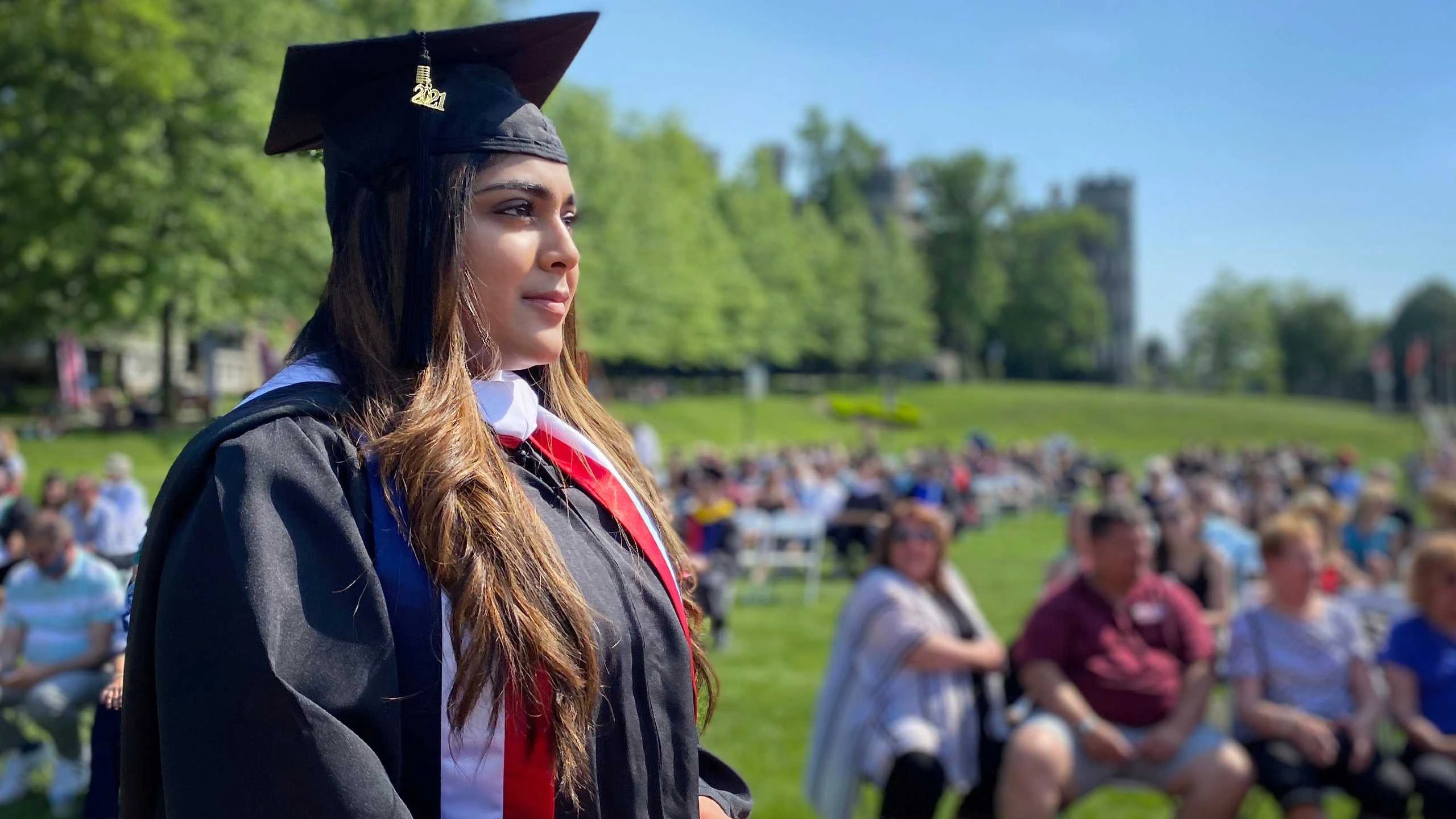A 2021 graduate stands proudly in the sun during a ceremony.