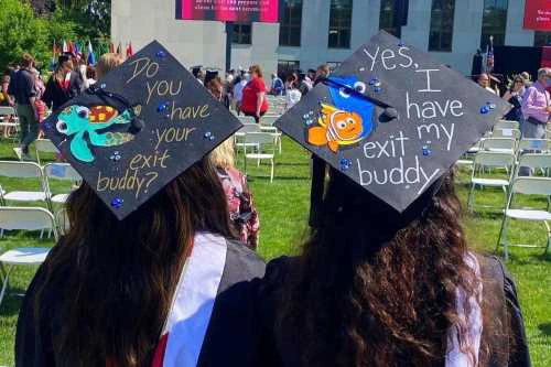 Two students wear fancy decorated caps during a graduation ceremony.