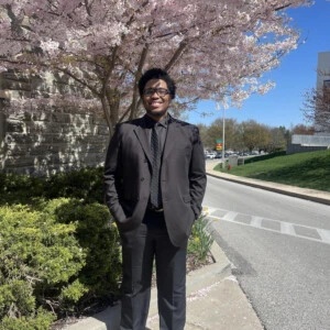 Oshane Mendez '24 wearing a suit and standing in front of a flowering tree