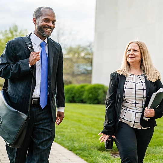Two graduate students walk by the library and hold business papers.