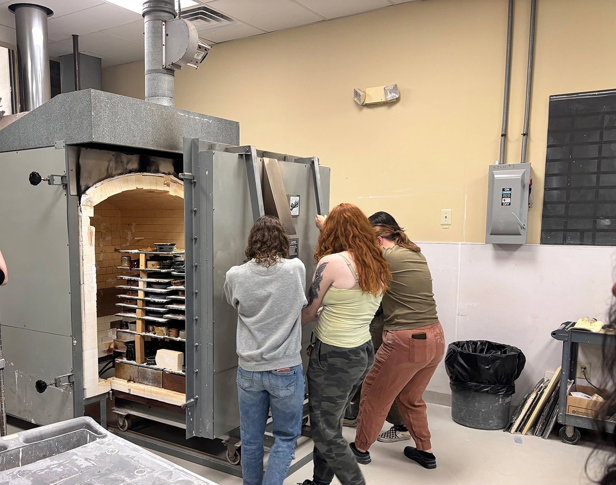 Three Arcadia students open the ceramics kiln so others can check their work.